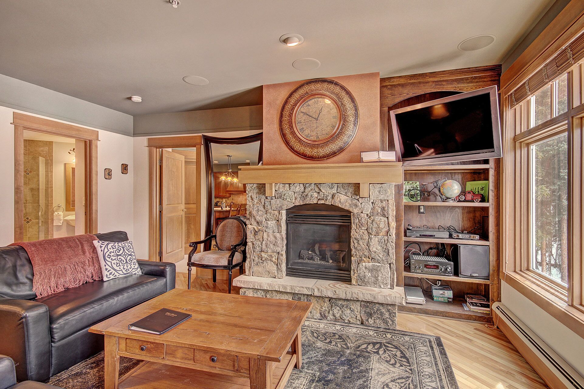 Una sala de estar con chimenea de piedra, un sofá de cuero, una mesa de centro de madera y un televisor sobre la chimenea.