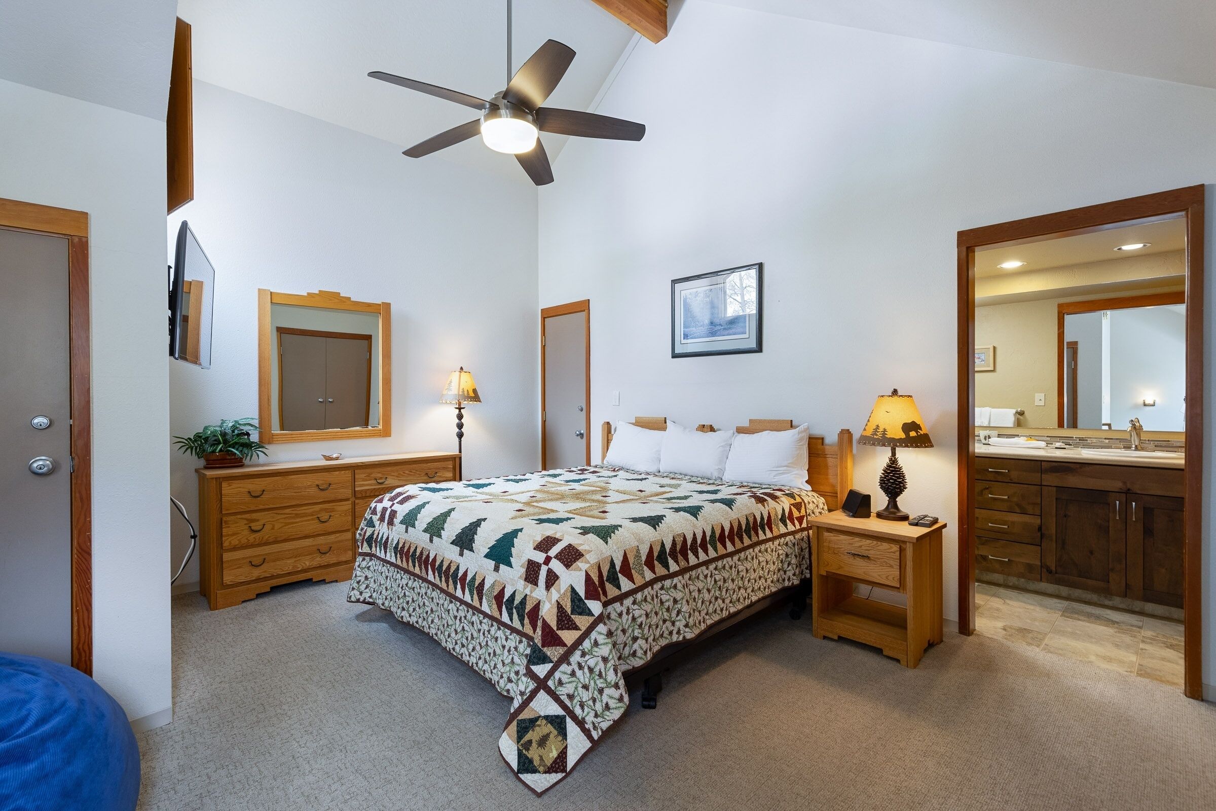 Un dormitorio con cama, cómoda de madera, mesita de noche, ventilador de techo y un espejo grande.