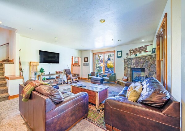 A spacious living room with leather sofas, a fireplace, a television, and a staircase.