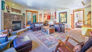 A spacious living room with a stone fireplace, leather sofas, a coffee table, and a patterned rug.