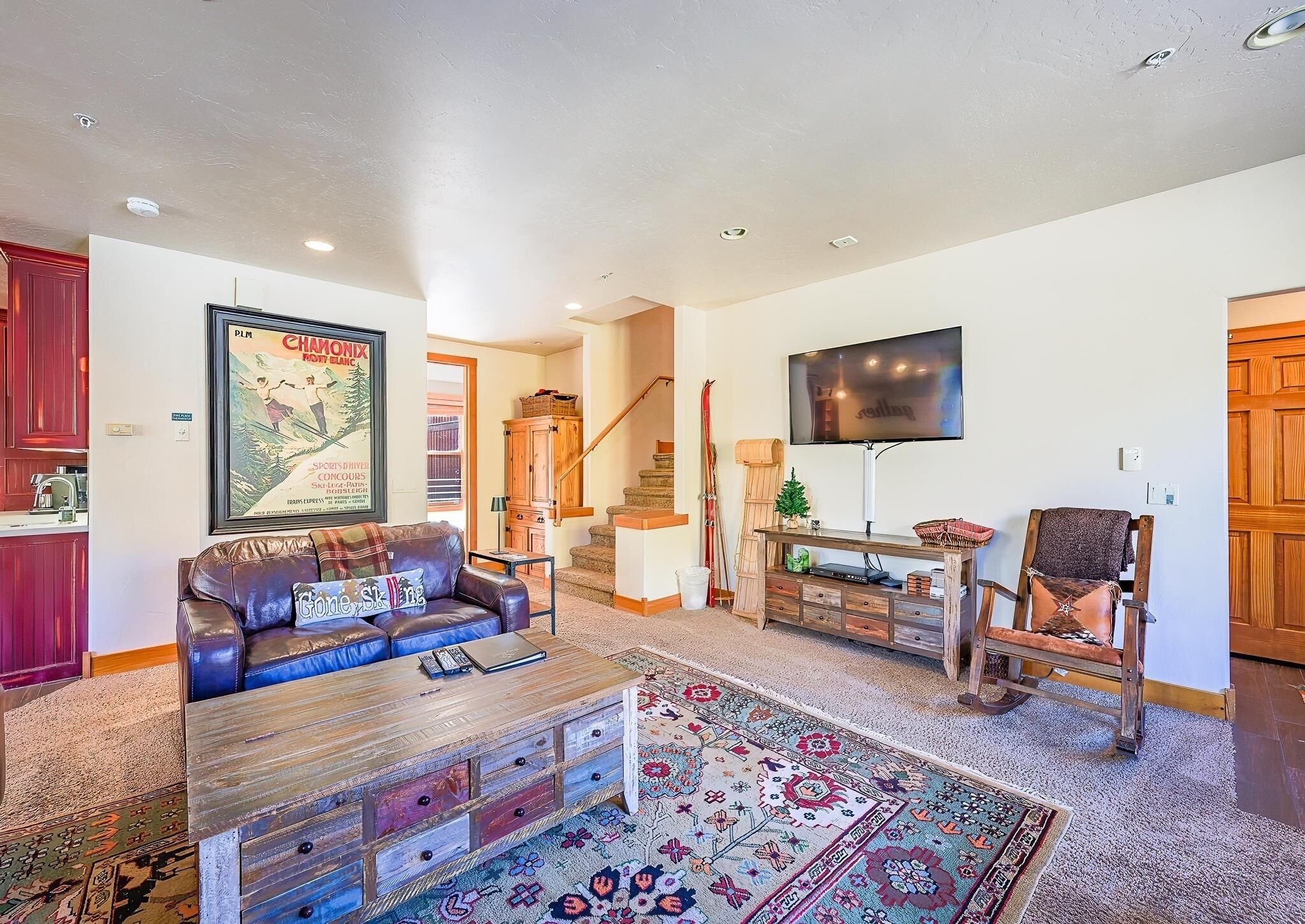 A spacious living room with a leather couch, a wooden coffee table, a flat-screen TV, and a staircase leading to another level.