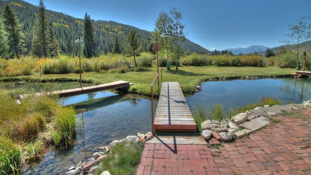 A wooden dock extending into a calm river, surrounded by lush greenery and a mountainous backdrop.
