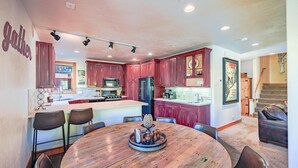 A modern kitchen with red cabinets, a central island, and a dining area with a wooden table and chairs.