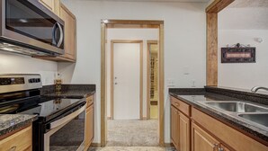 A kitchen with wooden cabinets, a microwave, a stove, and a sink. - 2062 The Pines 2 Bedroom Condo by RedAwning (Keystone)