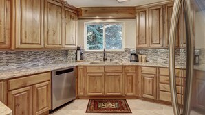 A kitchen with wooden cabinets, a stainless steel refrigerator, a window with a view of trees, and a tiled backsplash. - 221 Cinnamon Ridge I 2 Bedroom Condo by RedAwning (Keystone)