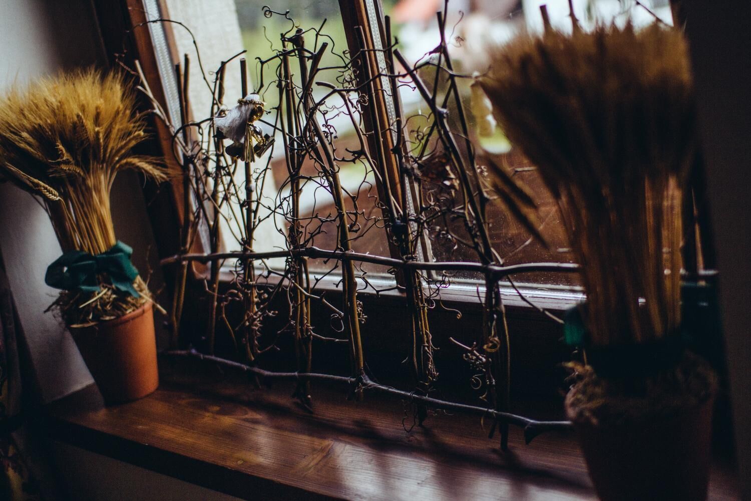 A window sill with various branches and dried plants, including a potted plant with a green bow.
