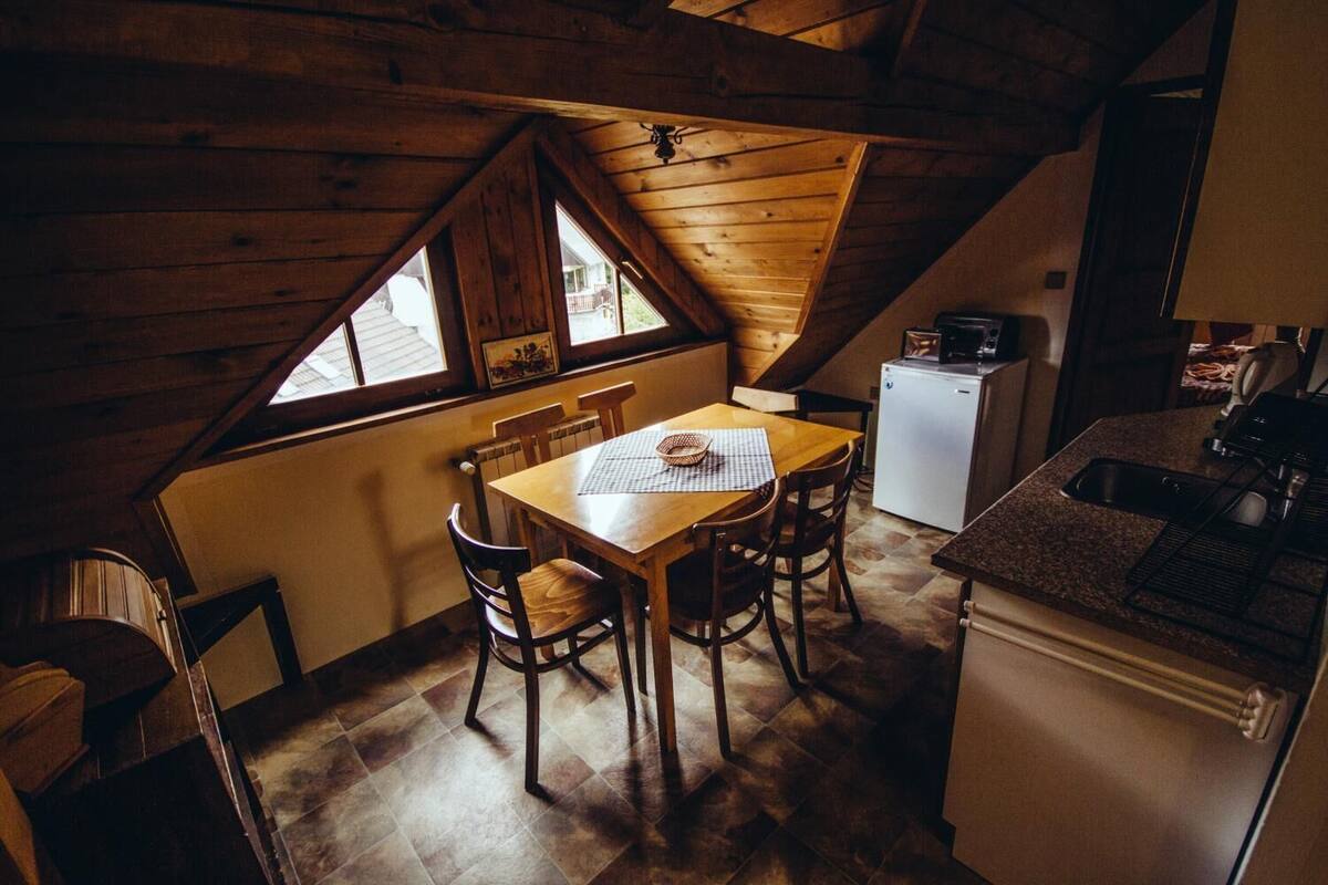 A cozy kitchen with a wooden table and chairs, a refrigerator, and a sink.