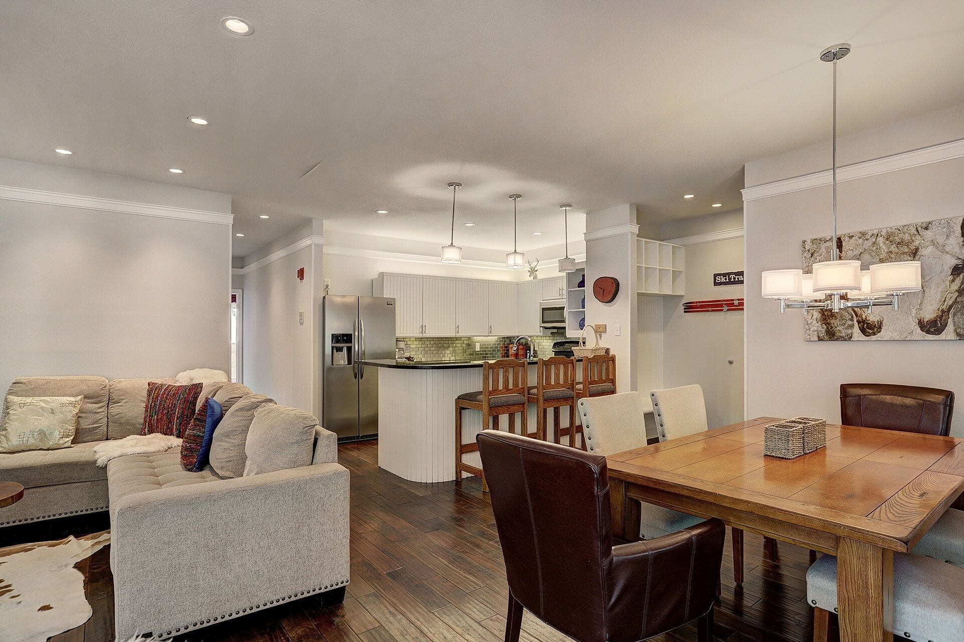 Una cocina moderna con armarios blancos, un refrigerador de acero inoxidable y un comedor con mesa y sillas de madera.