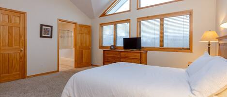 A bedroom with a large bed, wooden wardrobe, a TV on a dresser, and skylights.