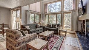 A spacious living room with a fireplace, large windows, and a patterned sofa. - 1655 Quicksilver 3 Bedroom Condo (Keystone)