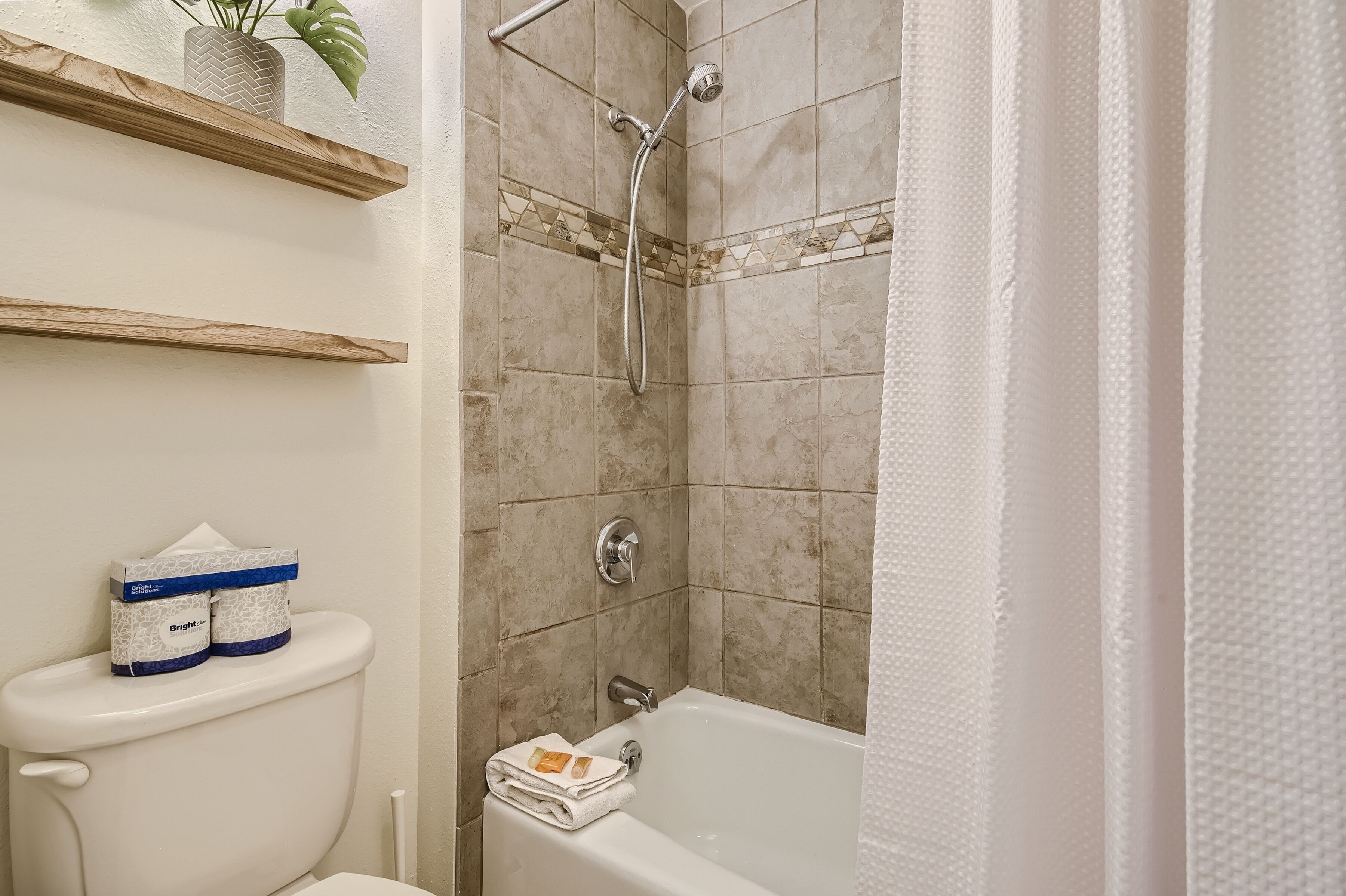 A bathroom with a toilet, a shower, and a bathtub. There are toilet paper and a towel on the toilet.