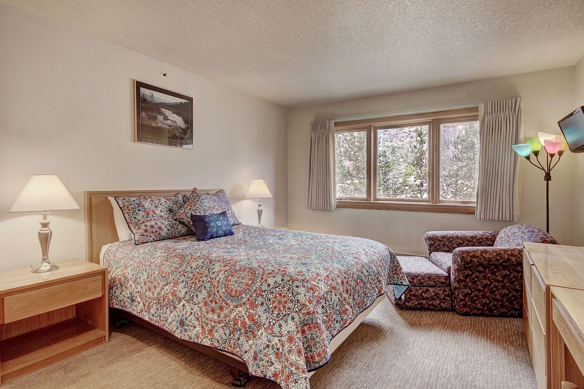 A bedroom with a bed, bedside tables, a desk, a chair, a window, and a lamp.