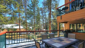 A deck with a table and chairs, surrounded by a railing, overlooking a forested area. - 1655 Quicksilver 3 Bedroom Condo (Keystone)