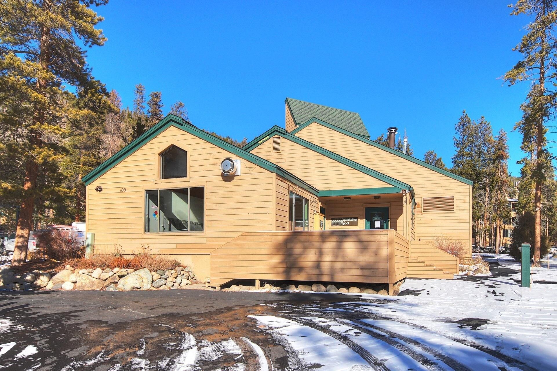 A wooden cabin with a green roof, a small porch, and a window.