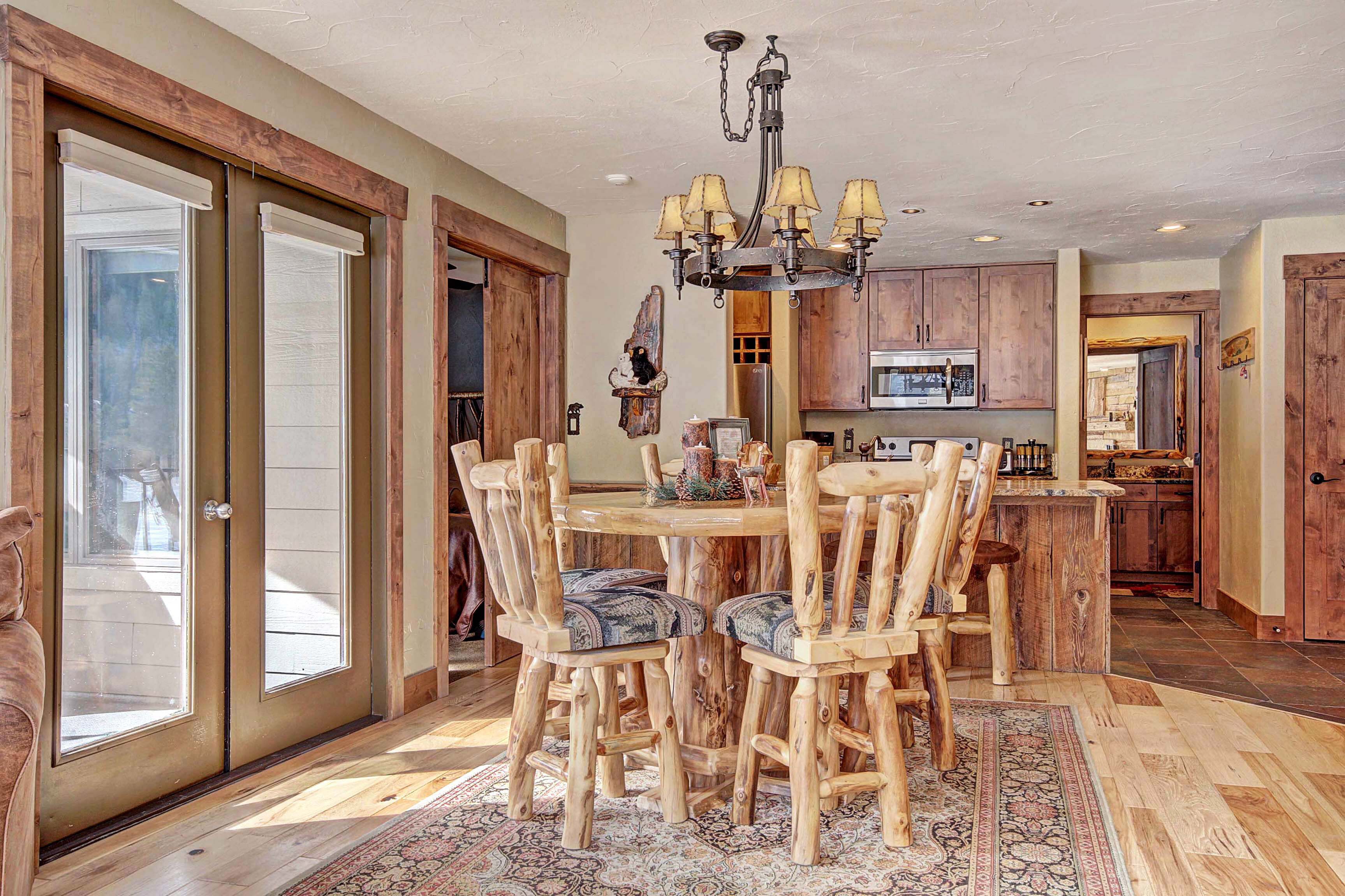 A dining area with a wooden table and chairs, a chandelier, and a view of the kitchen.