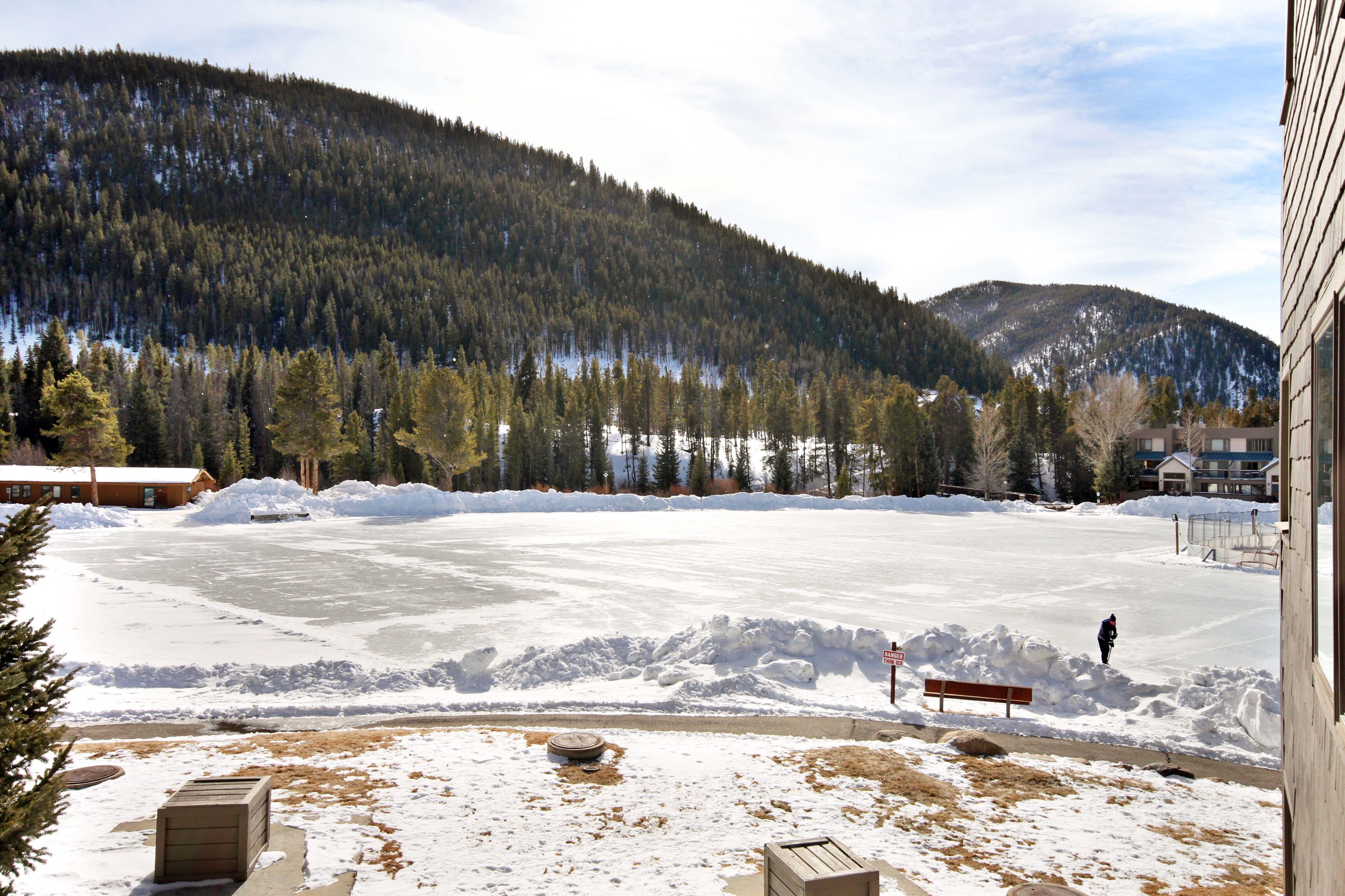 Vista de un lago congelado con una persona de pie a lo lejos, rodeada de nieve y árboles.