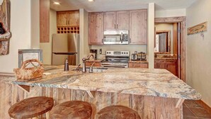 A kitchen with wooden cabinets, a central island with stools, a refrigerator, a microwave, and a stove.