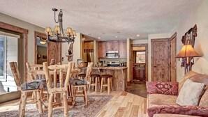 A rustic kitchen with wooden cabinets, a central island, and a dining area with wooden chairs.