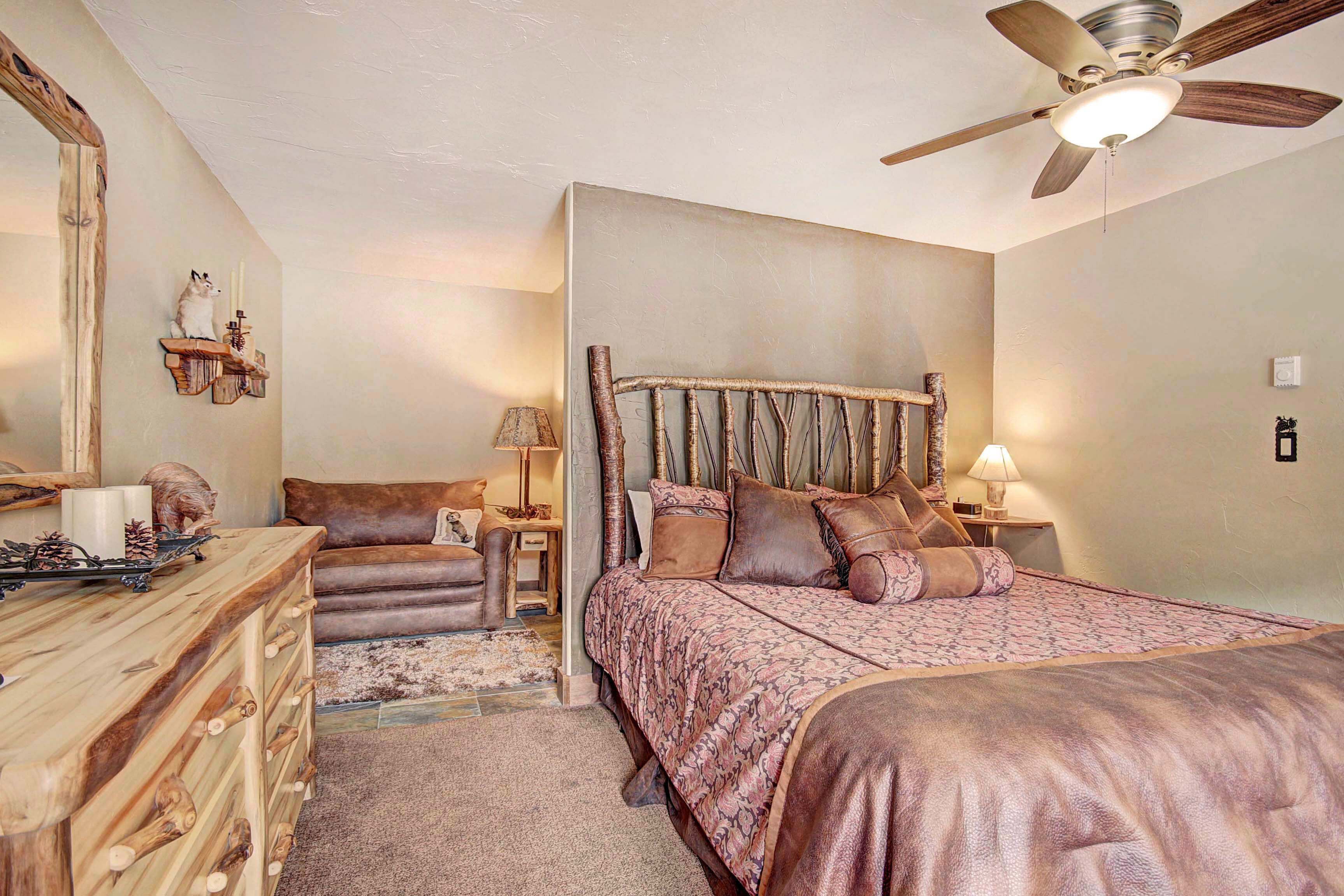 A bedroom with a large bed, a wooden dresser, a chair, and a ceiling fan.