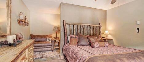 A bedroom with a large bed, a wooden dresser, a chair, and a ceiling fan.