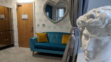 Una habitación con un sofá color turquesa, un armario de madera, un espejo con marco en forma de corazón y una escultura de busto blanco.