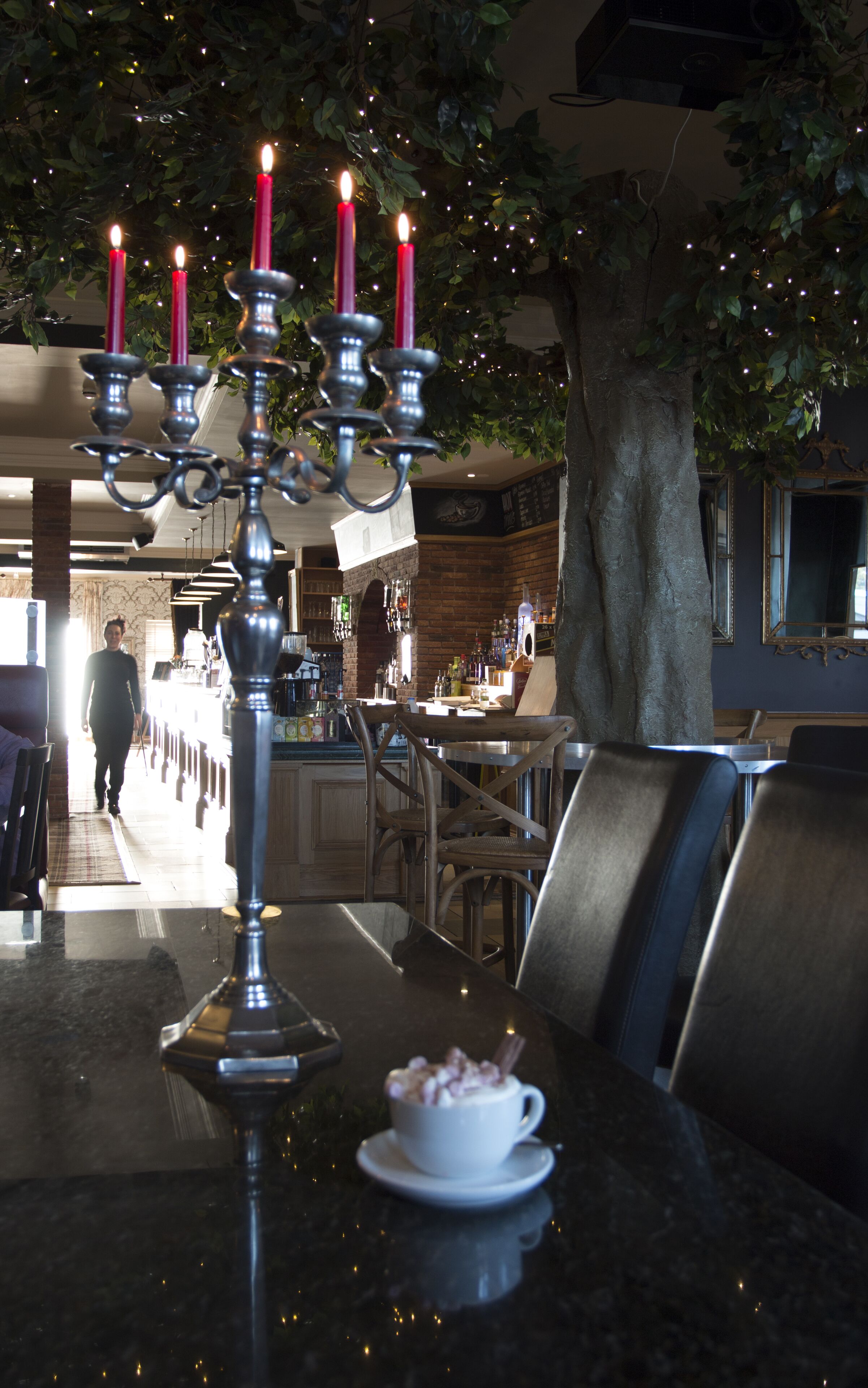 A dining area with a table set for two, a candelabra with lit candles, and a tree in the background.