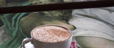 Une tasse de café posée sur une soucoupe, avec une cuillère, le tout placé sur une table devant laquelle on aperçoit un tableau.
