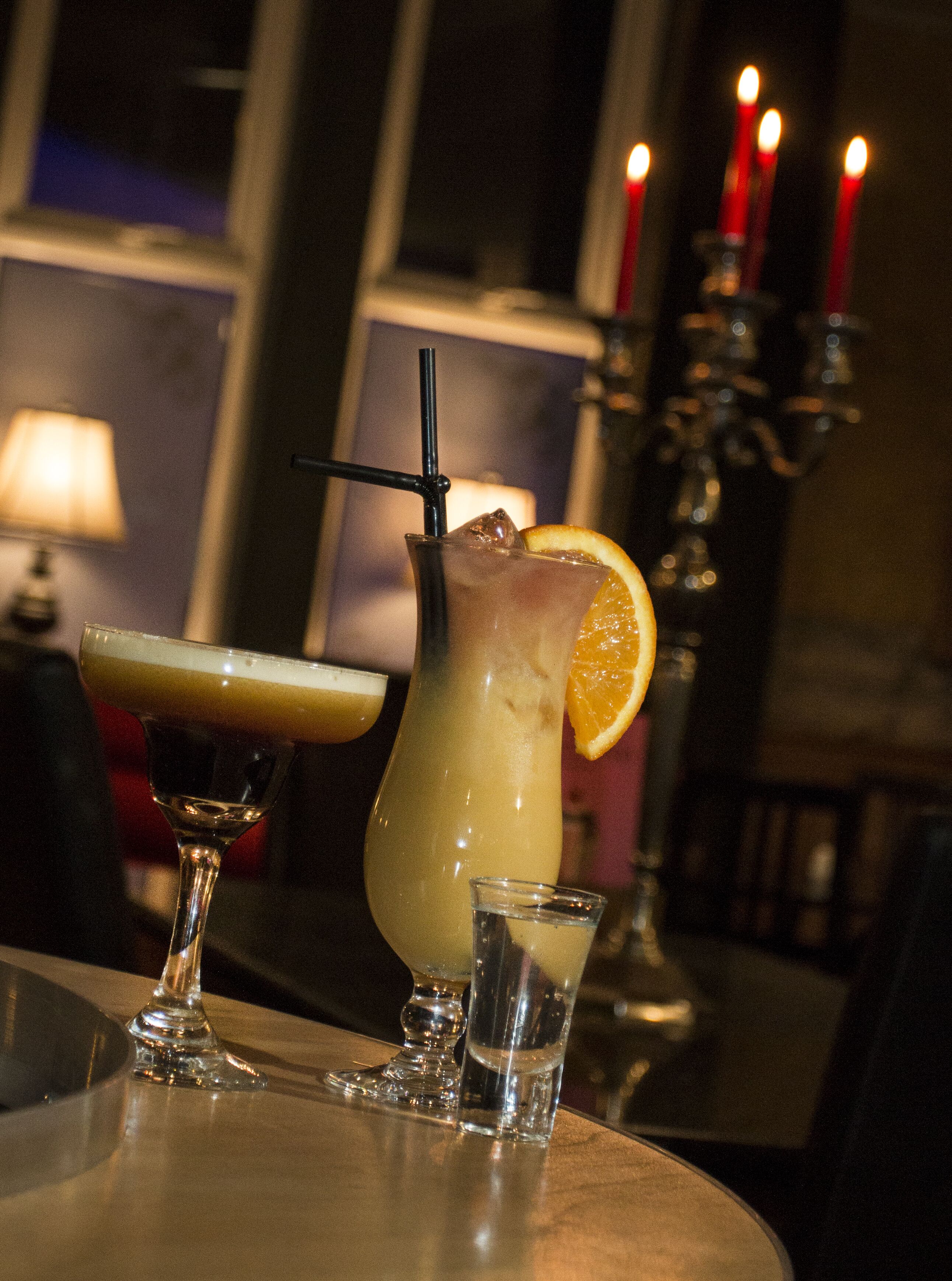 Un bar con dos bebidas, un candelabro y una lámpara al fondo.
