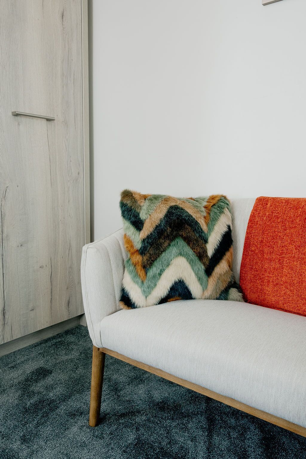 Ein weißes Sofa mit einem farbenfrohen Kissen mit Zickzackmuster und einem schlichten orangefarbenen Kissen.