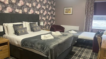 A hotel room with a bed, a chair, a table, and a window with curtains.