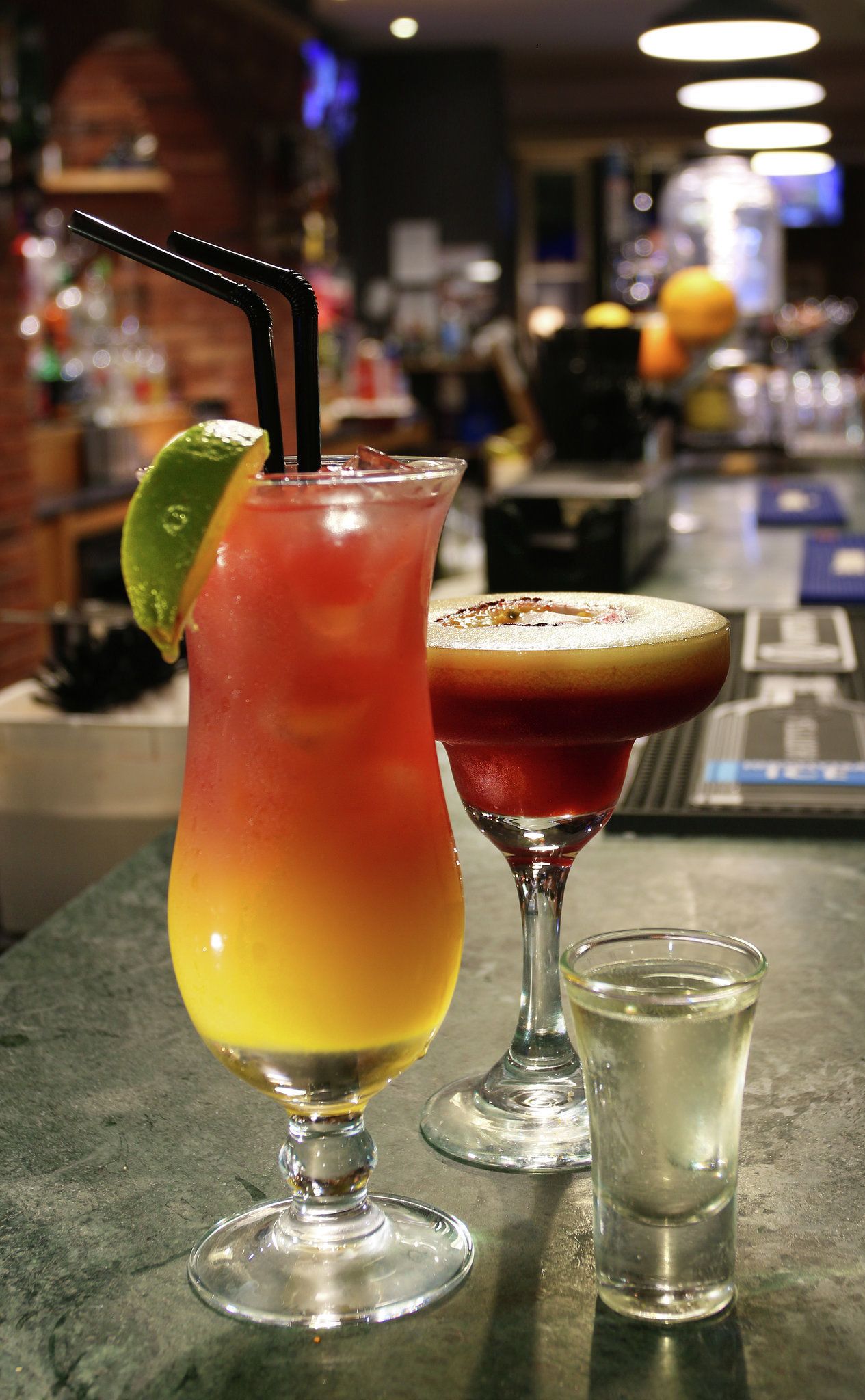 Kaksi cocktail-lasia baaritiskillä, jokaisessa limenviipale ja pilli.