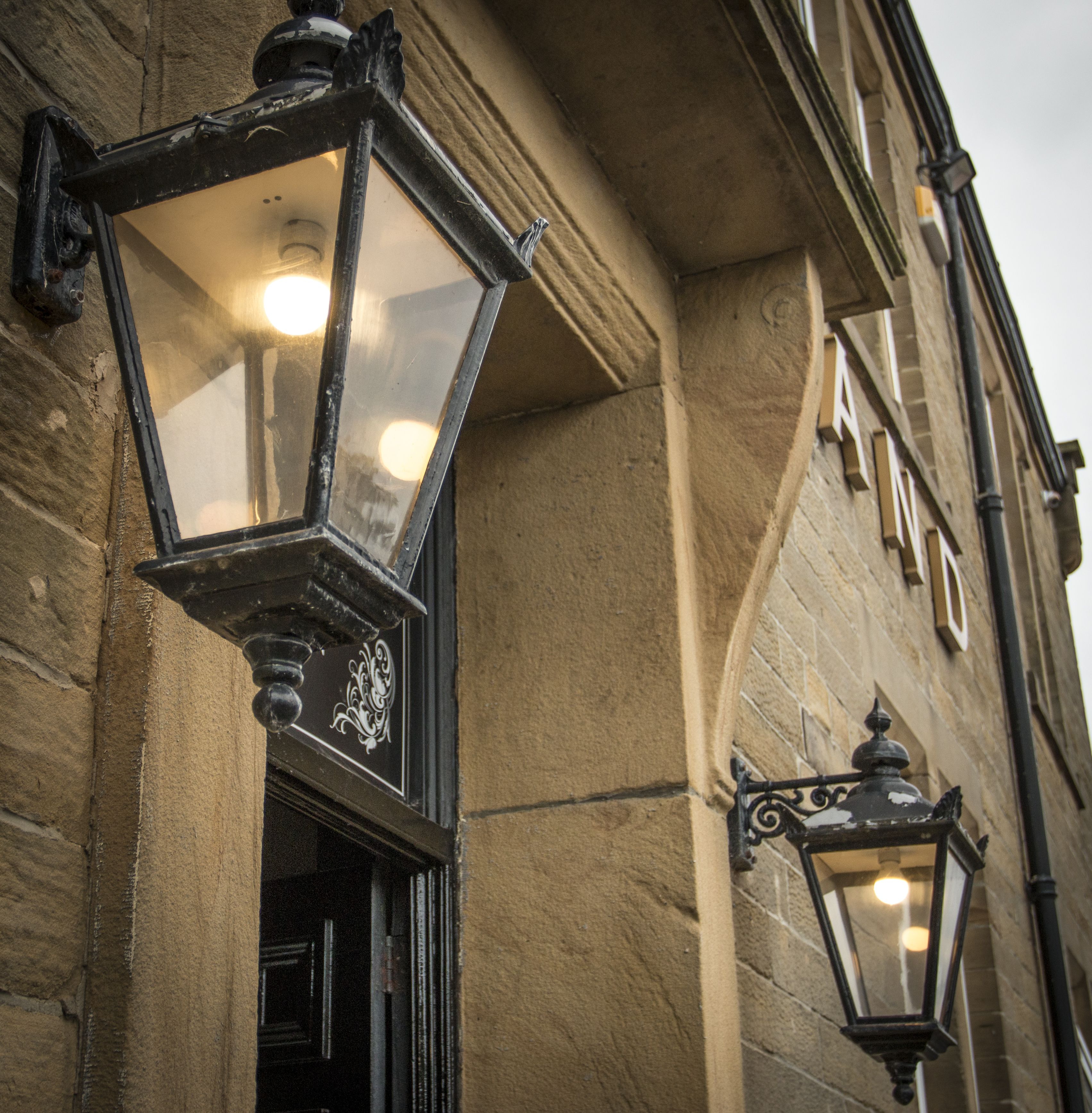 Une façade d’immeuble avec un revêtement extérieur en pierre, une porte et deux lampadaires décoratifs.