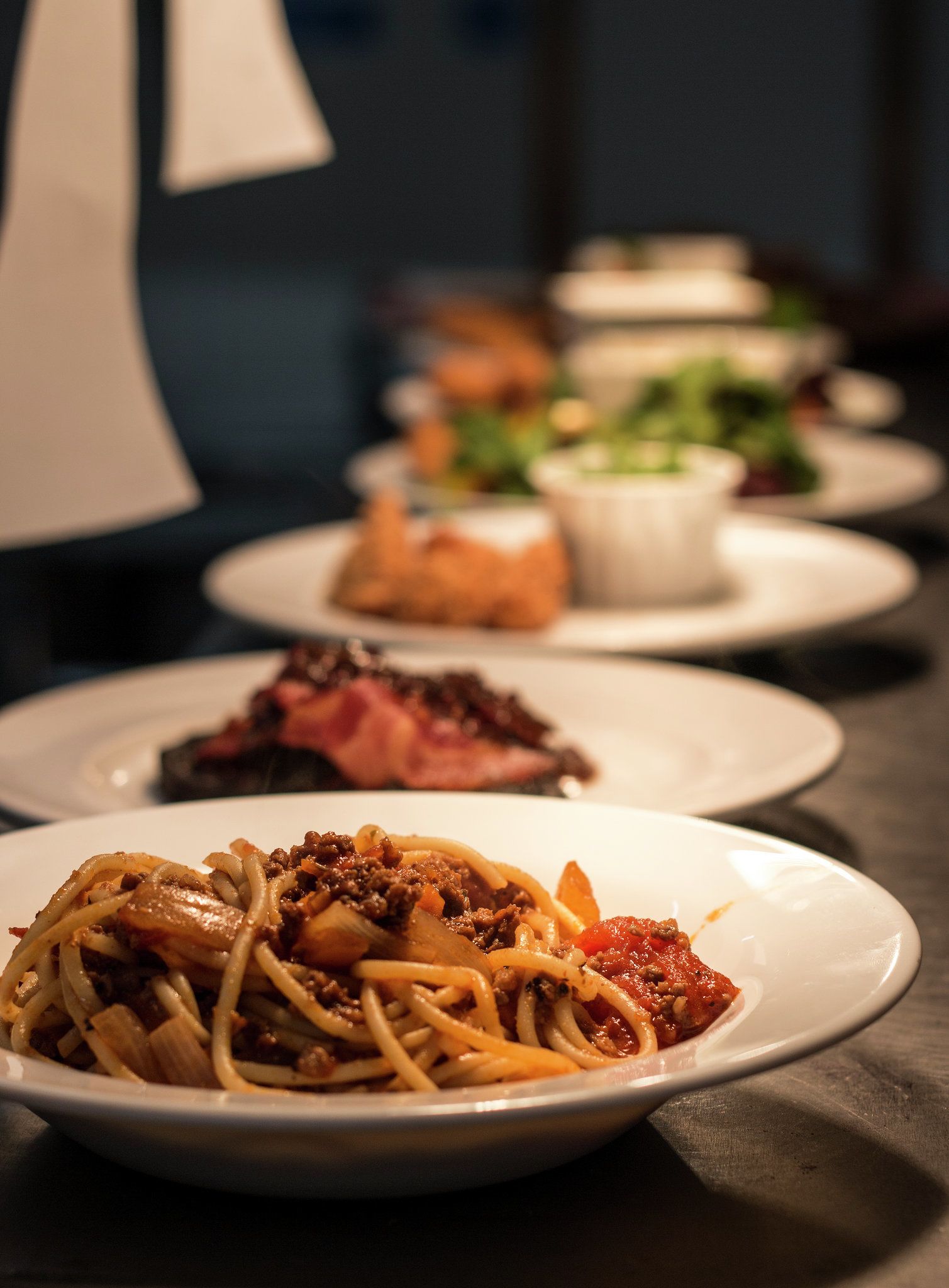 Une table garnie de différents plats, notamment des spaghettis à la viande et aux légumes, ainsi que d’autres assiettes contenant divers aliments.