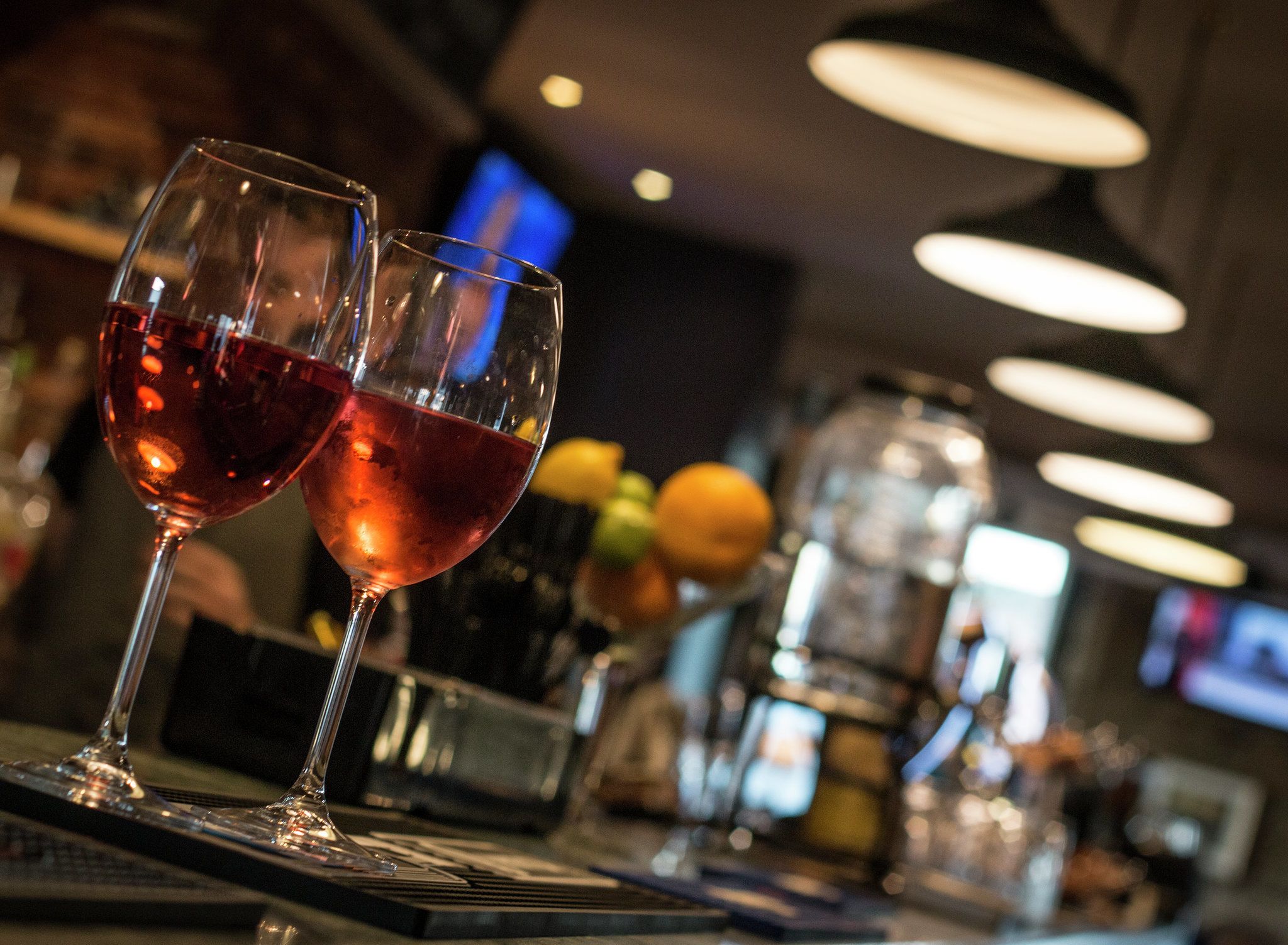 Deux verres de vin rouge sur le comptoir d’un bar, avec un arrière-plan flou représentant le bar et quelques fruits.