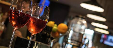 Deux verres de vin rouge sur le comptoir d’un bar, avec un arrière-plan flou représentant le bar et quelques fruits.