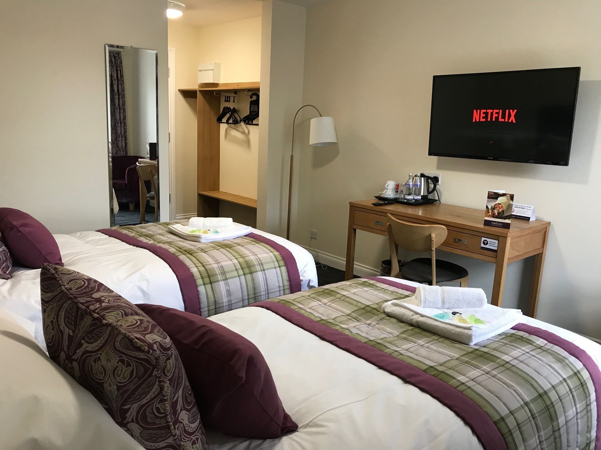 A hotel room with two beds, a desk, a chair, a TV, and a coat rack.