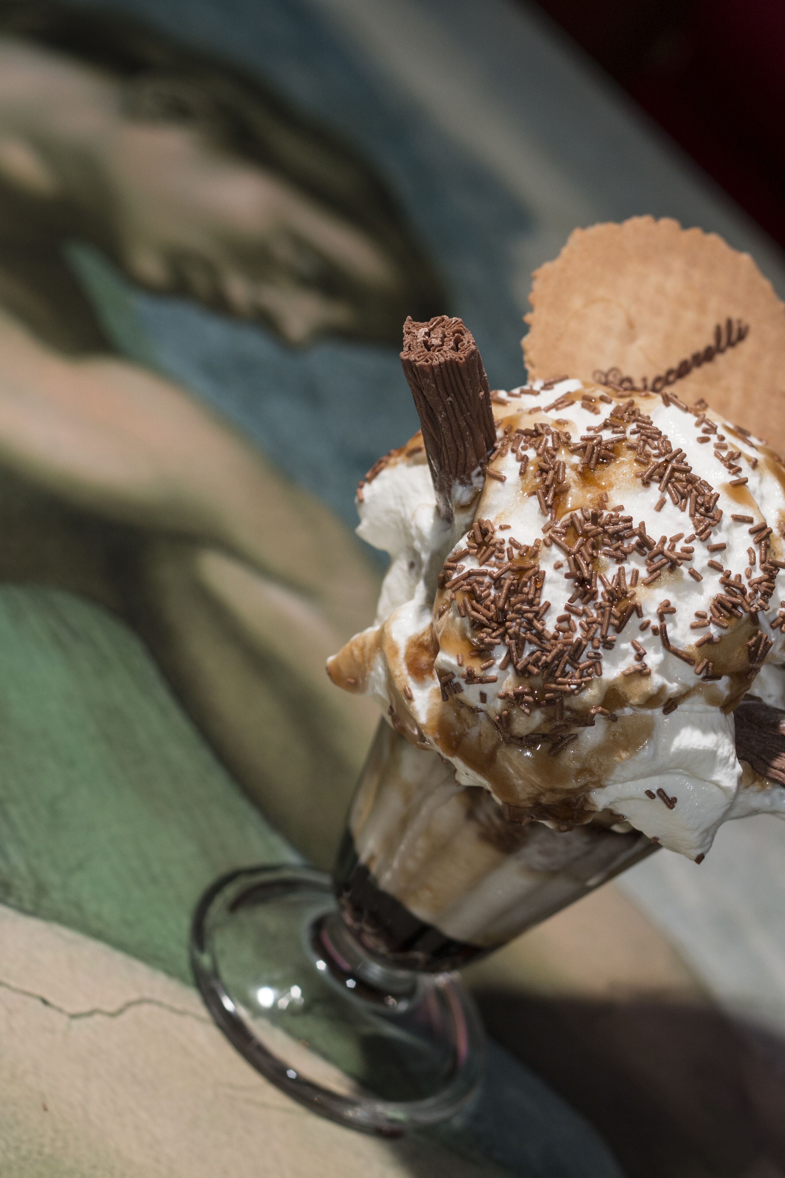 Uma sobremesa em copo com um palito de chocolate e granulado por cima.