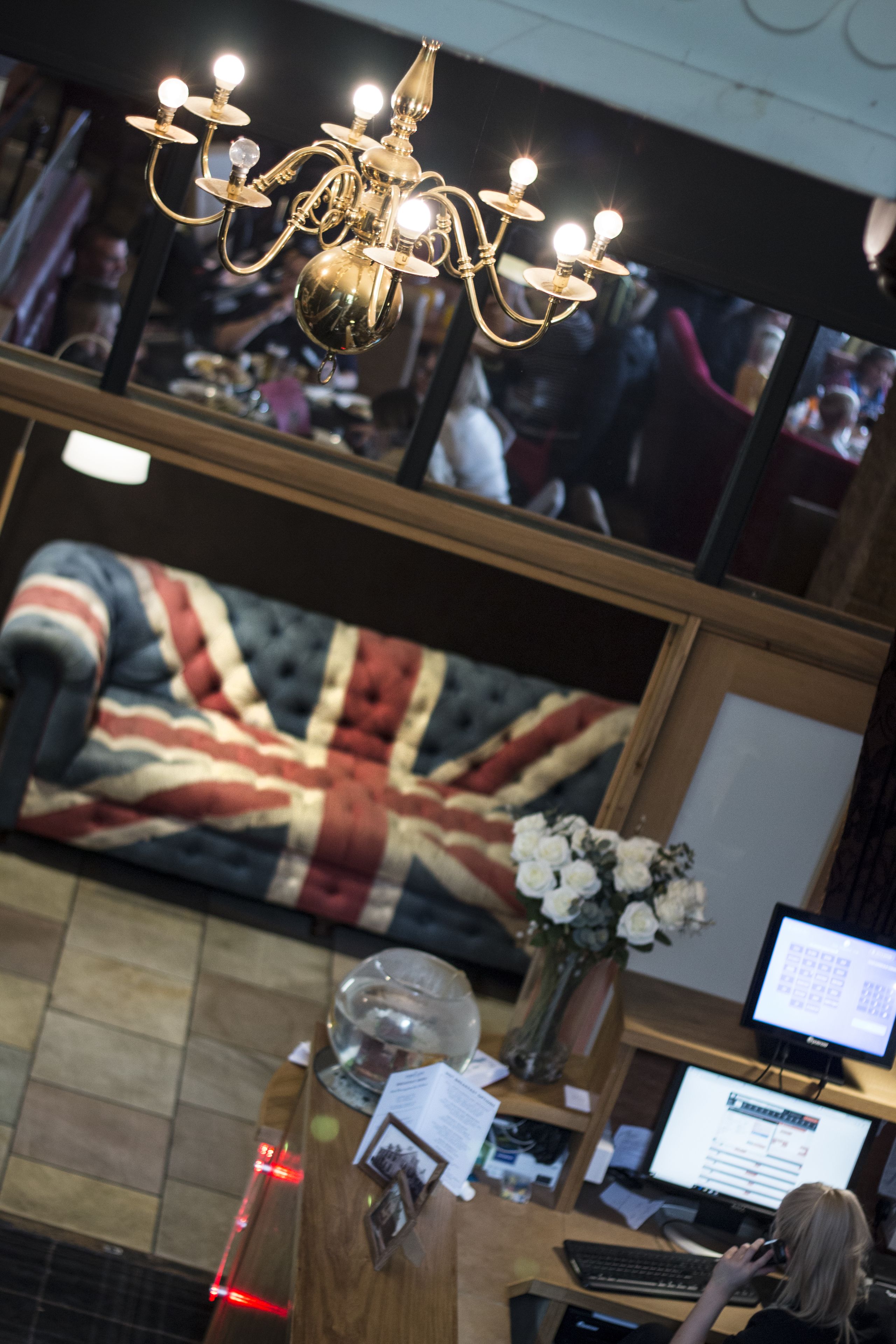 A hotel lobby with a chandelier, a British flag-patterned sofa, a reception desk, and a computer monitor.