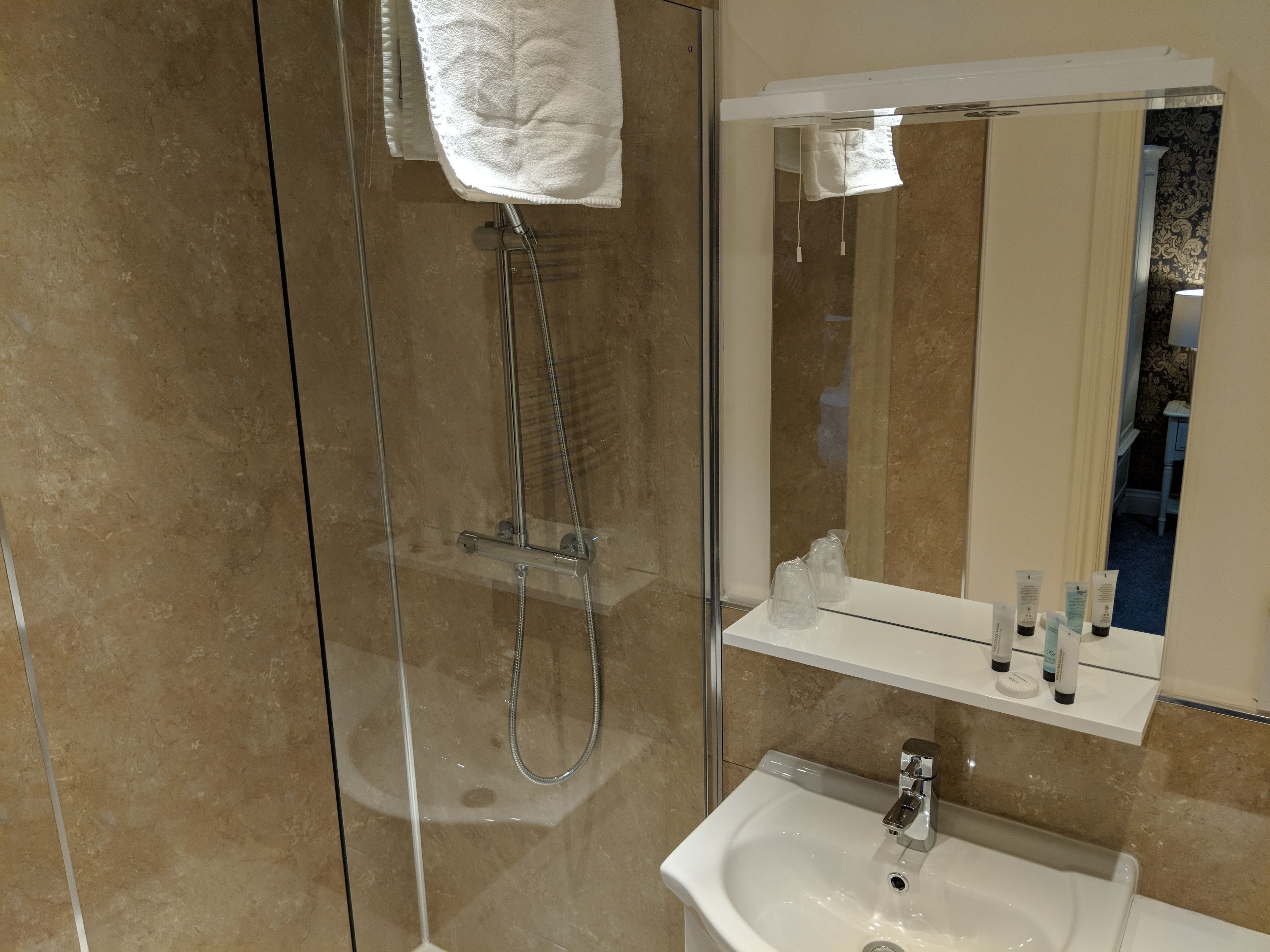 A modern bathroom with a glass-enclosed shower, a white sink, and a mirror above a shelf with toiletries.