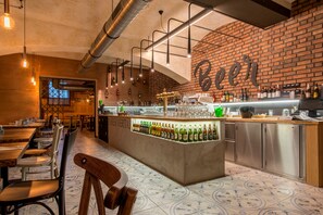 Una zona de bar con pared de ladrillo, una barra con botellas y asientos con sillas y mesas.
