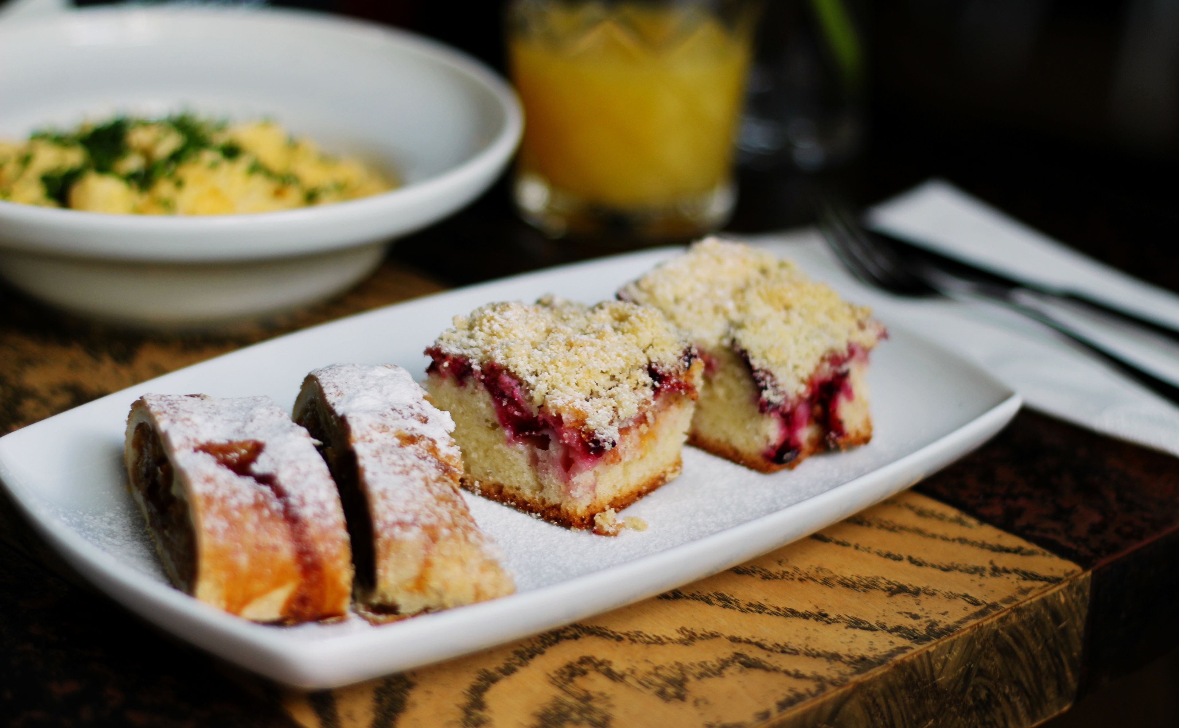 A white rectangular plate with three pieces of cake on a wooden table.