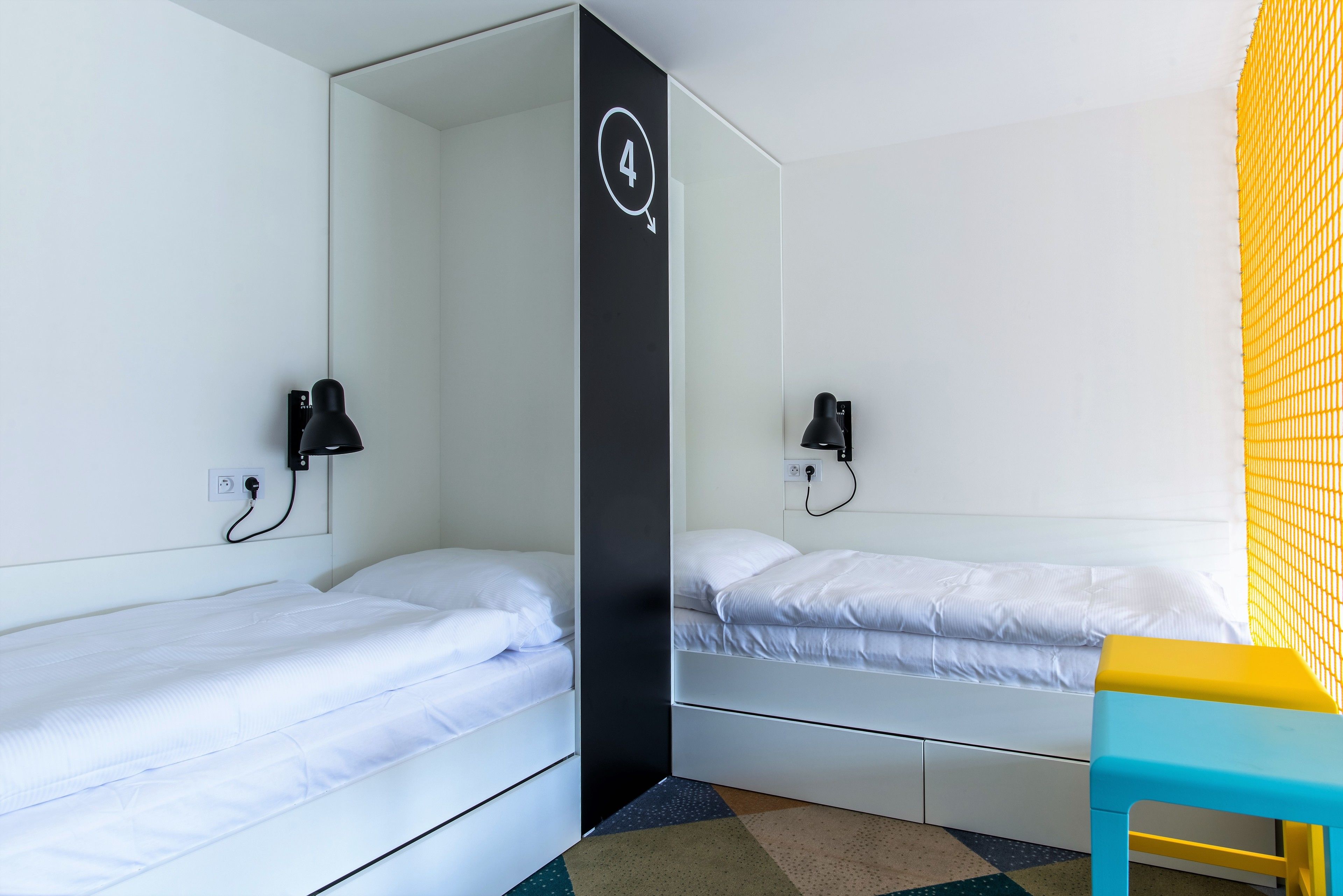 Una habitación con dos camas individuales, un pilar negro con un número y una silla amarilla.