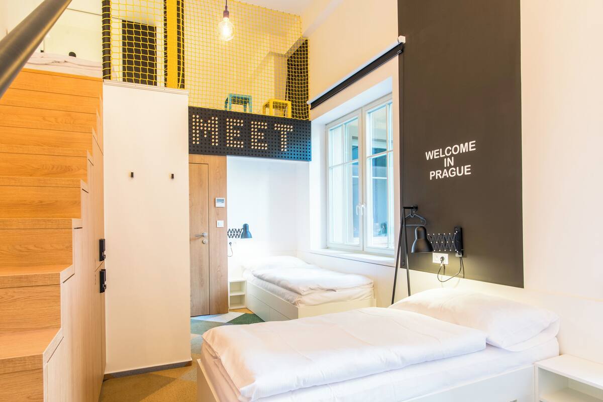 A modern hotel room with a bed, a desk, a chair, a window, and a staircase.