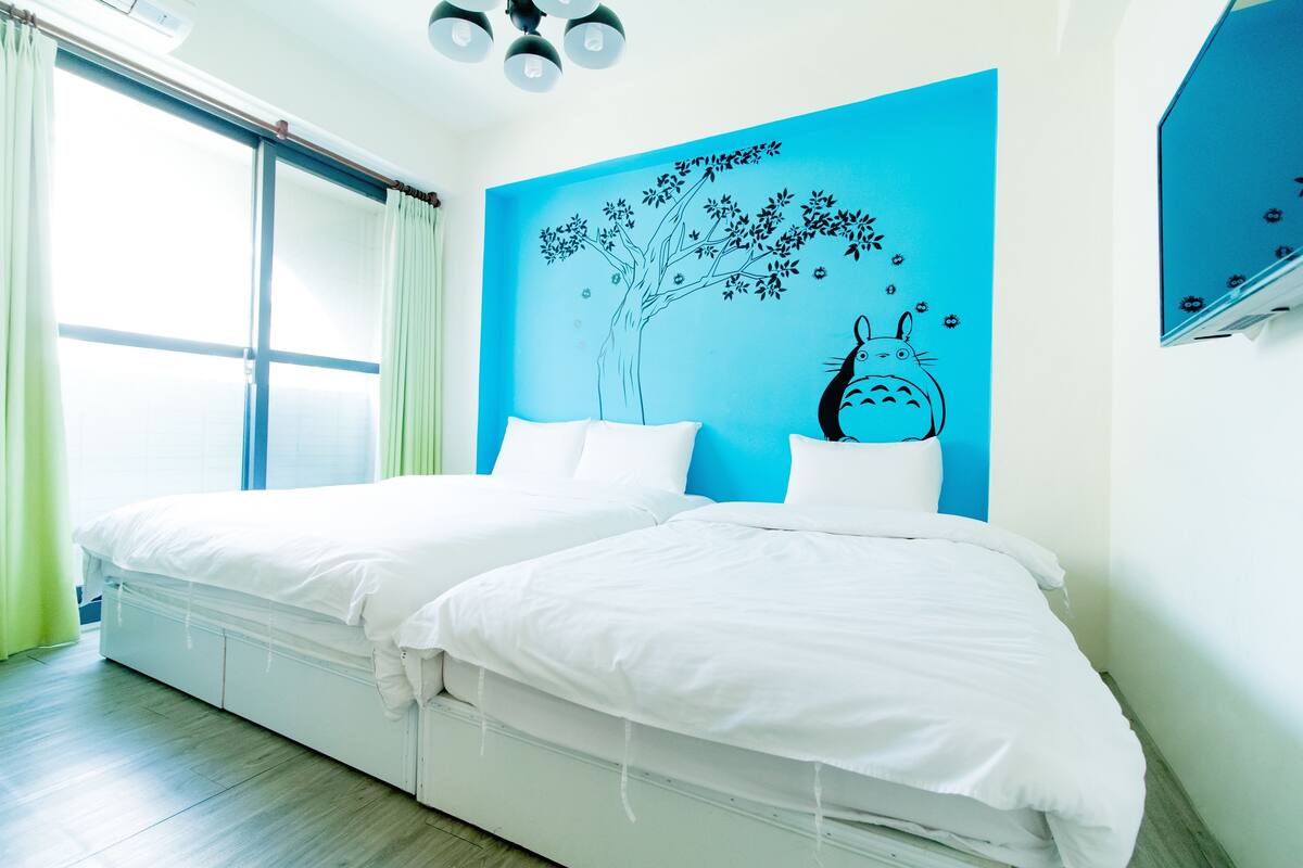 Ein modernes Hotelzimmer mit zwei Betten, einem großen Fenster und einer blauen Wandmalerei.
