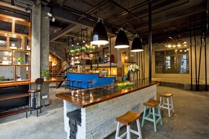 A bar area with a central island, stools, and shelves with plants.
