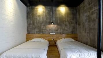 A room with two single beds, a wooden headboard, a concrete wall, and a hanging light fixture.