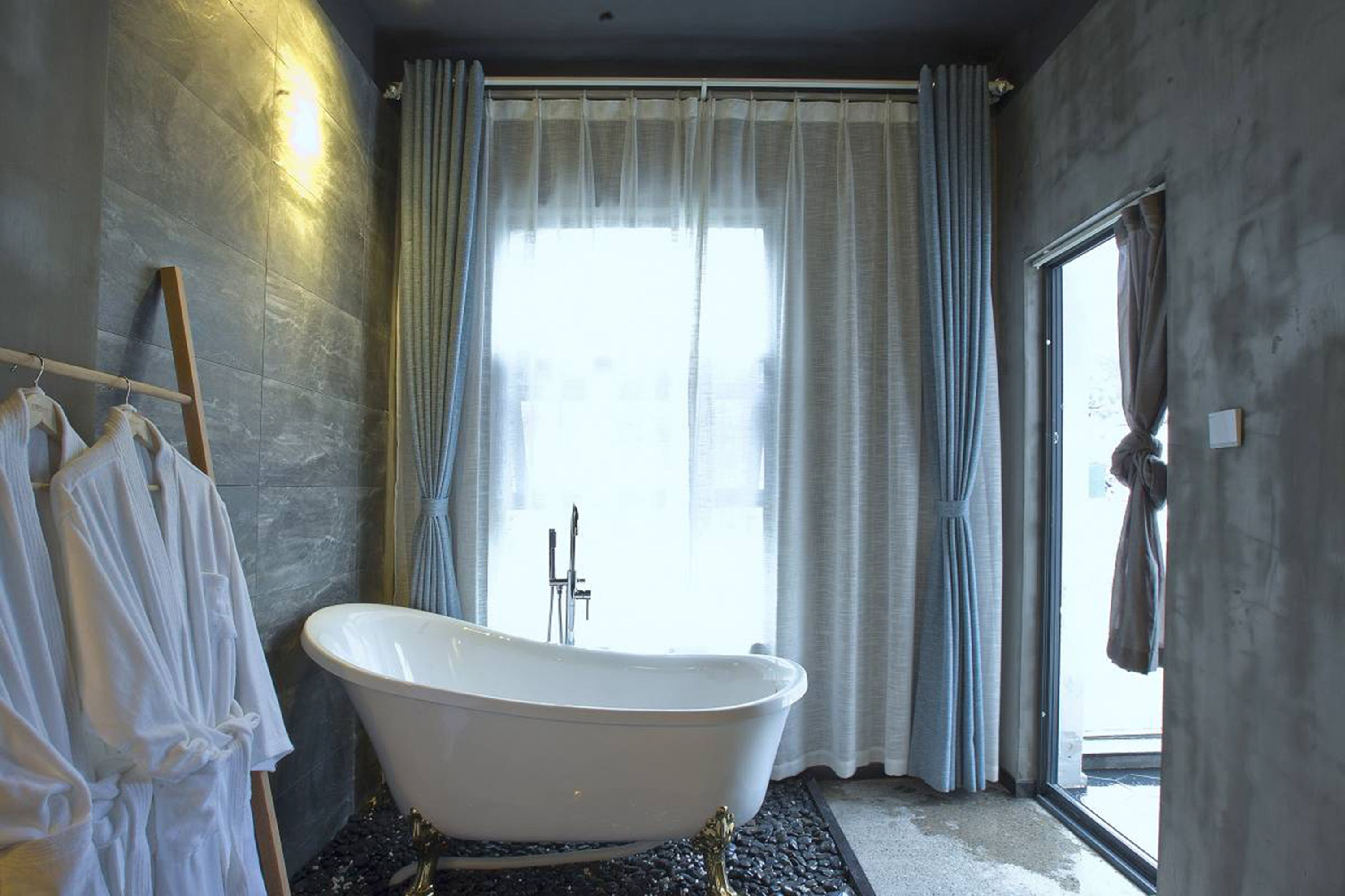 Une salle de bain avec une baignoire sur pieds, un porte-serviettes avec des serviettes blanches et une fenêtre avec des rideaux.