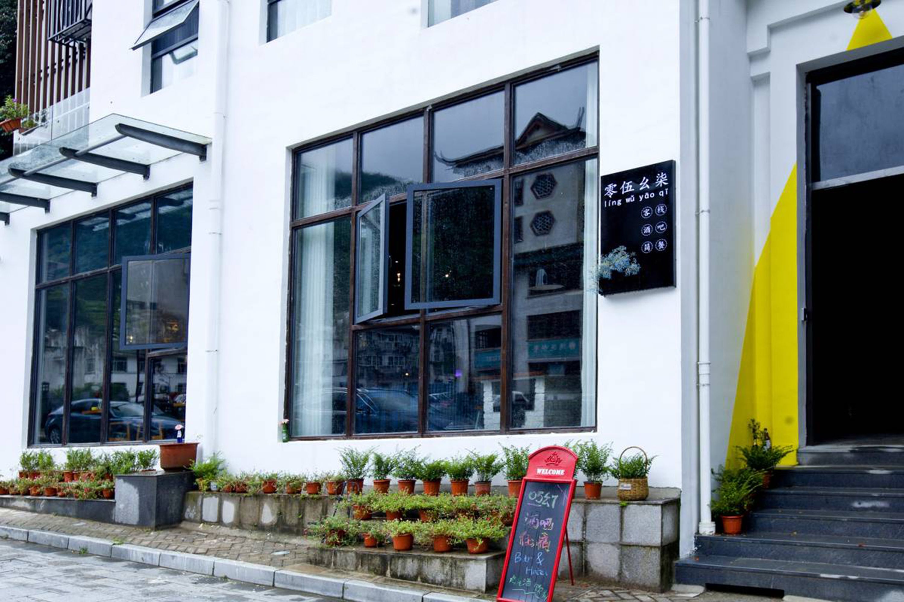A building with large windows, a blackboard sign, and potted plants outside.