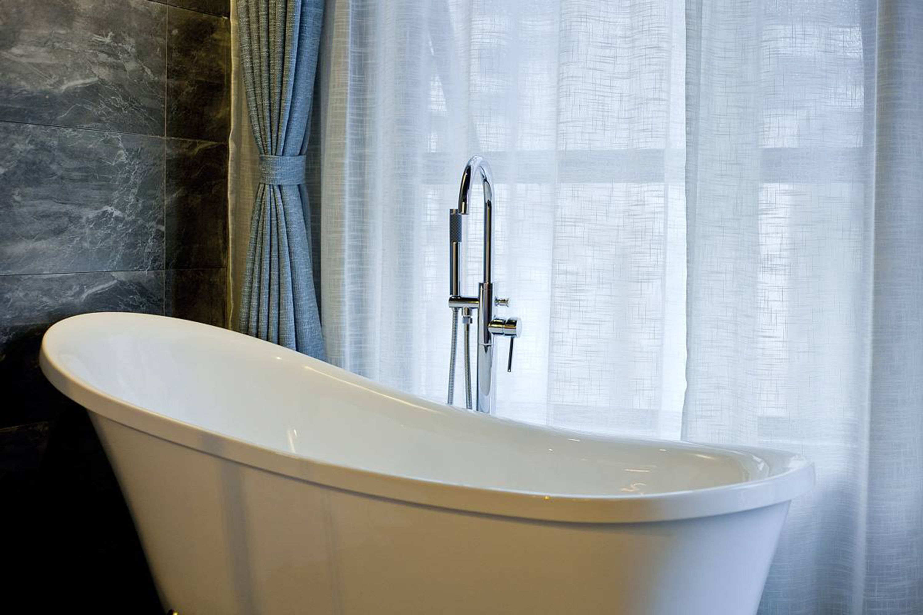 Un baño moderno con una bañera independiente, cabezal de ducha y una cortina.