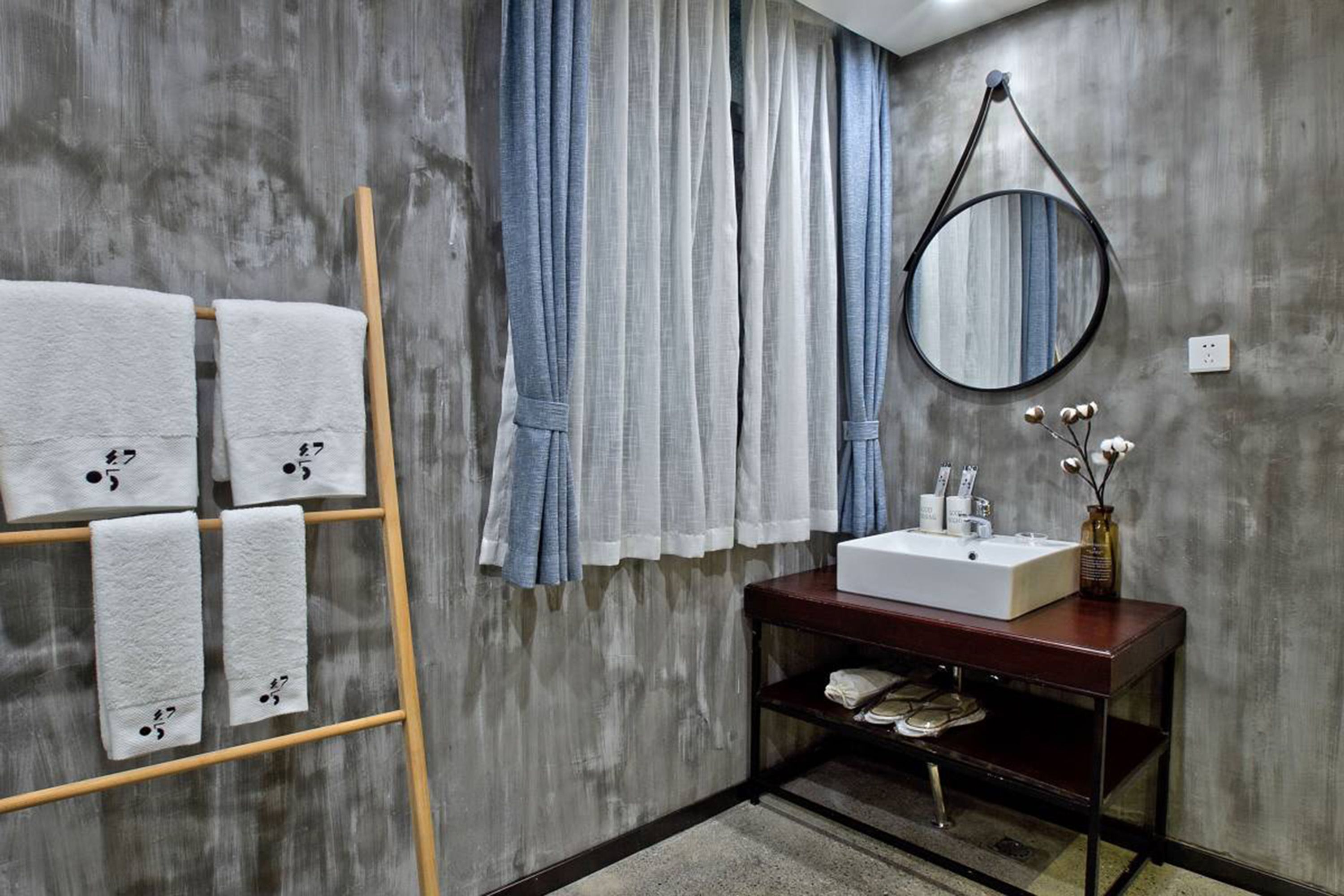 A bathroom with a wooden towel rack holding four towels, a sink with toiletries, and a mirror on the wall.